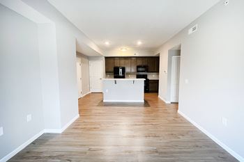 An empty living room and kitchen with white walls and wood flooring